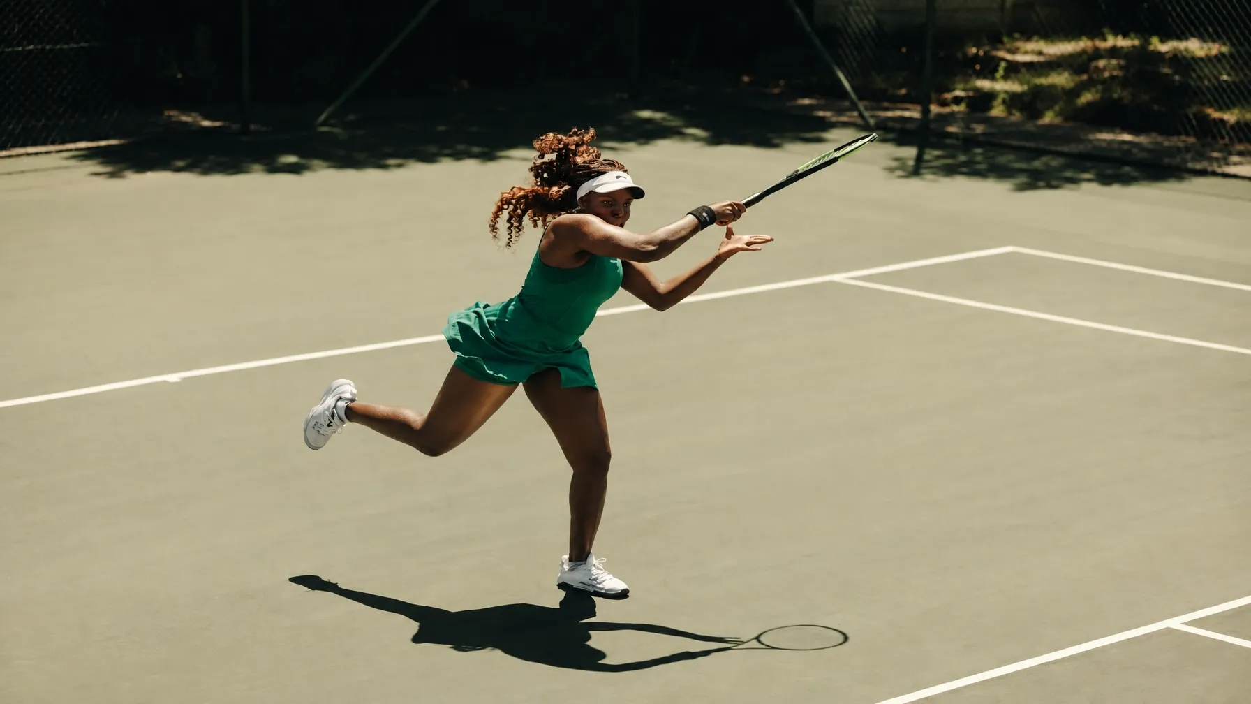 A tennis player mid-swing on a sunlit hard court